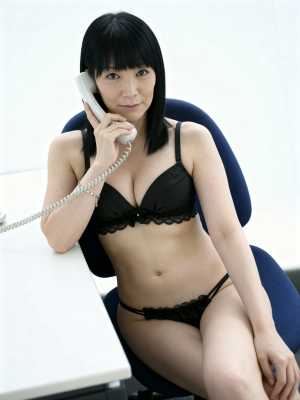 黒いレースのブラとお揃いのパンティーを身に着け、机に座って電話をしている女性を正面か...。