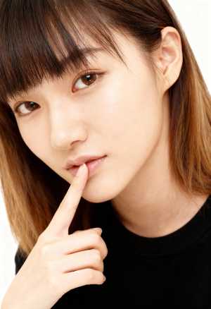 指を唇に押し当ててポーズをとる、思慮深い表情をした若い女性の接写。