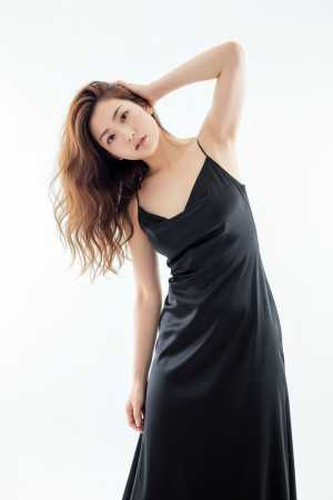 真っ白な背景に自信を持ってポーズをとる黒いロングドレスを着た若い女性を横から撮った写...。