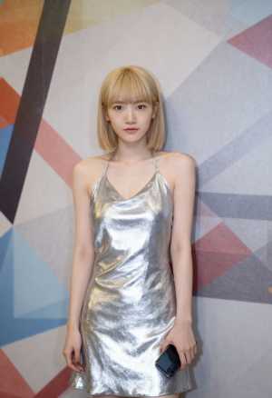 光沢のあるシルバーのドレスを着て、幾何学模様の壁の前に立っている若い女性を正面カメラ...。