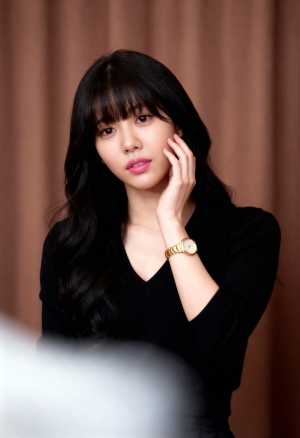 ウェーブのかかった長い黒髪と前髪を持ち、黒い V ネックのセーターと金の時計を着てい...。