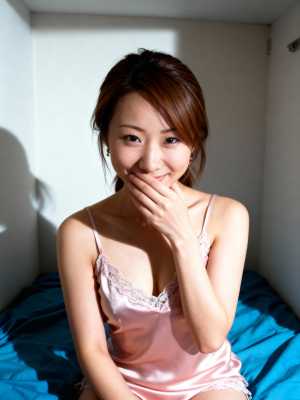 明るい色の壁と青い毛布のあるシンプルな部屋のベッドに座っている若い女性を、正面カメラ...。