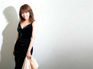 黒のベルベットのフォーマルなドレスを着て、真っ白な壁に立ち、左手にベージュの布を持っ...。