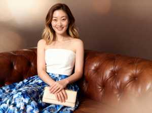 白いストラップレスのトップと青い花柄のスカートを着て、リラックスしたポーズで茶色の革...。