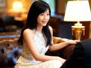 豪華なホテルのロビーで茶色の革張りのソファに座り、白いビーズのドレスを着た若い女性。