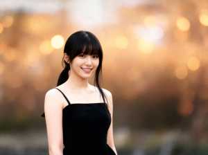 画像の中央に黒いドレスを着た、陽気な表情をした若い女性の写実的なポートレート。