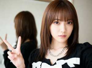 茶色の長いストレートの髪と前髪を持ち、白いリボンが付いた黒いセーターを着て、銀のチェ...。