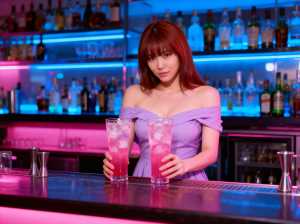 ピンクの飲み物が入った背の高いグラスを 2 つ持ち、バーの後ろに立っている若い女性を...。