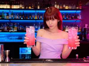 バーの後ろに立ち、ピンク色の飲み物が入った背の高いグラスを 2 つ持っている若い女性...。