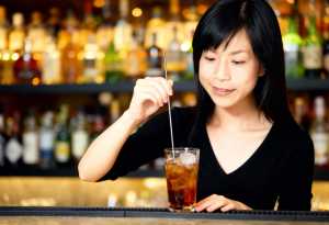 黒いVネックのシャツを着た長い黒髪の若いアジア人女性が、酒瓶の棚を背景にした薄暗いバ...。