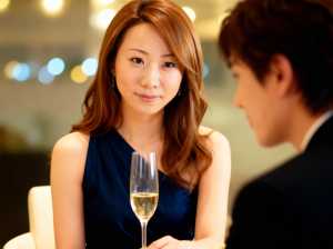 ネイビーブルーのノースリーブのドレスを着て、白ワインのグラスを前にテーブルに座ってい...。