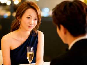 ネイビーブルーのワンショルダードレスを着てシャンパンを飲みながらテーブルに座り、正装...。