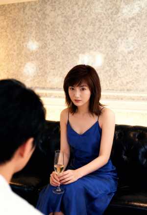 青いドレスを着て黒い革張りのソファに座り、白ワインのグラスを持った若い女性を正面から...。