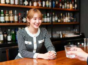 白い襟と金ボタンが付いた黒と白の千鳥格子のジャケットを着て、バーカウンターにグラスを...。