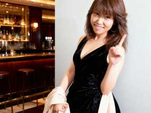 黒いベルベットのドレスを着た若い女性が画像の中央に立ち、自信に満ちた笑顔で親指を立て...。