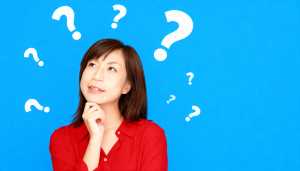 明るい青色の背景に疑問符で囲まれた、思慮深い表情を持つ若いアジア人女性のポートレート。