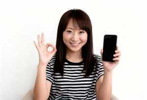 画像の中央に座っている若いアジア人女性は、右手に黒いスマートフォンを持ち、左手で「O...。