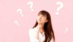 白いブラウスを着た長い茶色の髪の若い女性が、画像の中央に顎を乗せて座り、思慮深い表情...。