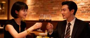 薄暗いレストランのテーブルに座り、ワイングラスで乾杯する男女のロマンチックなシーン。