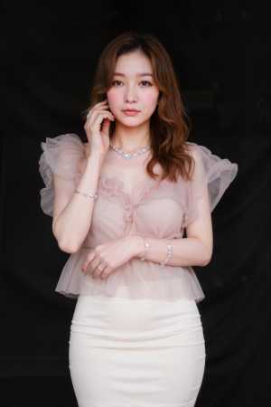 フリル袖のシアーピンクのトップスと白いペンシルスカートを着て、黒い背景に自信を持って...。