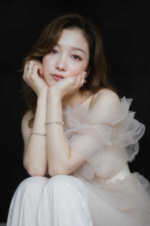 薄手のオフショルダーのトップと繊細なブレスレットを身に着け、あごに手を当てて瞑想的に...。