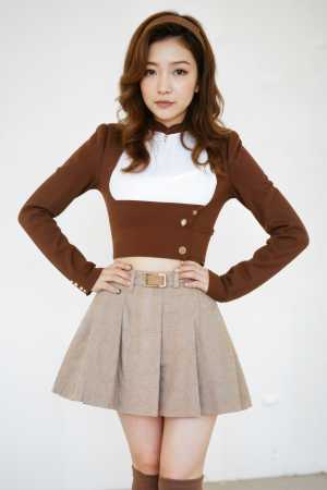 無地の白い壁の前で腰に手を当てて自信満々にポーズをとるアジア系の若い女性。