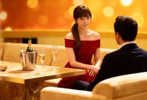 赤いオフショルダーのドレスを着た若い女性が、フォーマルなスーツを着た男性とテーブルに...。