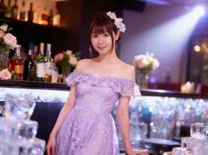 ボトルと花を背景にバーの前に立つ、薄紫のドレスを着た若い女性を正面カメラのアングルか...。