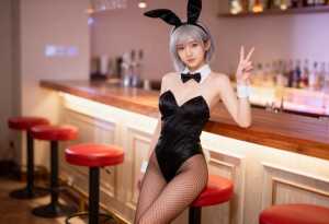 ウサギの格好をしてバーに座り、右手でピースサインをしている若い女性を横から撮った写実...。