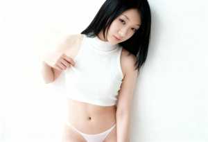 白いリブ編みのノースリーブトップスとそれに合ったパンティーを着て、無地の白い壁に向か...。