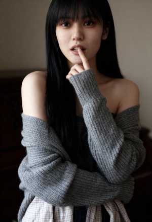 グレーのオフショルダー セーターとチェックのスカートを着て、唇の近くに指を当ててポー...。