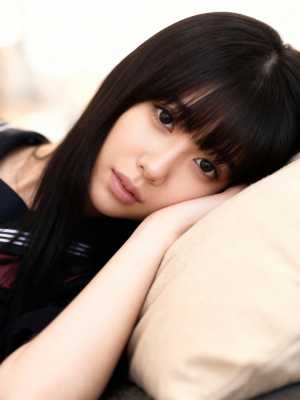 長く真っ直ぐなダークブラウンの髪と前髪を持ち、ベージュの枕にあごを乗せている若い女性の接写。