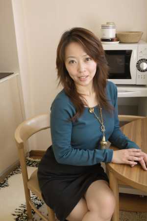 青いセーターと黒いスカートを着て、居心地の良いキッチンのテーブルに座っている若い女性...。