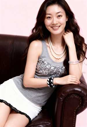 スパンコール付きのタンクトップと白いスカートを着て、茶色の革張りのソファにリラックス...。