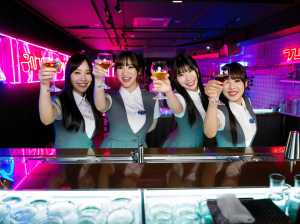 バーカウンターの後ろに立っている 4 人のアジア人女性が、それぞれ異なる色の飲み物の...。