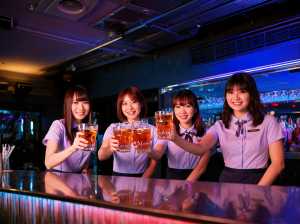 バーの後ろに立ち、ビールのグラスを手にカメラに向かって微笑む 4 人の若い女性を正面...。