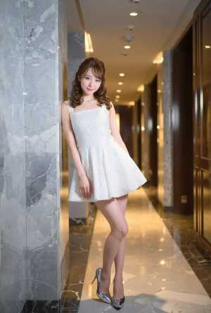 モダンな廊下の大理石の壁に立っている白いドレスを着た若い女性を横から撮影した写実的な写真。