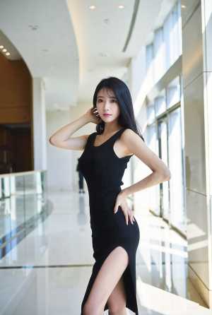 サイドにスリットの入ったタイトな黒のドレスを着て、モダンな建物で自信を持ってポーズを...。