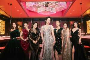 高級宝石店に立ち、大きなピンクのシャンデリアの前で写真を撮る 7 人の女性のグループ。