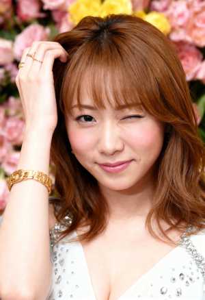 ピンクと黄色の花を背景にポーズをとる、ウェーブのかかった茶色の長い髪と温かい笑顔を持...。