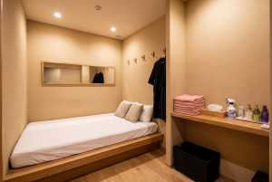 部屋の中央にシングルベッド1台、木のフレームと白いリネンを配した、ミニマルなデザイン...。