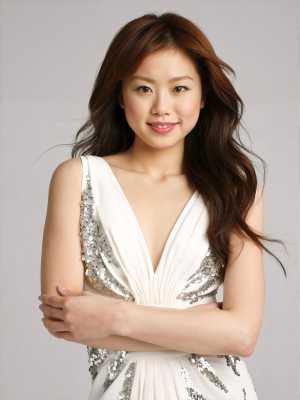 長くウェーブのかかった茶色の髪をした若いアジア人女性が、銀のスパンコールで飾られた白...。