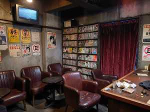 ヴィンテージ感のある薄暗い部屋で、手前に赤い革張りの椅子と木製のテーブルが置かれています。