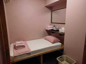 ピンクの壁と中央にシングルベッドが置かれたミニマルなベッドルーム。