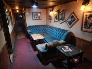 薄暗い部屋の中央に青いベルベットのチェスターフィールドソファがあり、その両側に小さな...。