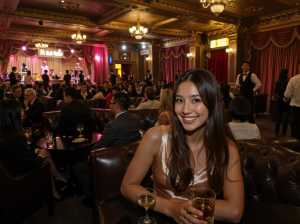 高級レストランのテーブルに座り、カメラに向かって微笑む女性。