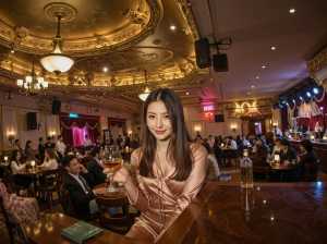 豪華で華やかなレストランで大勢の人々に囲まれ、バーに座ってワインを持っている女性を正...。