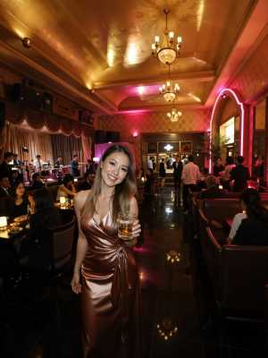 高級レストランでビールのグラスを持ち、カメラに向かって微笑む女性を正面から写実的に撮...。