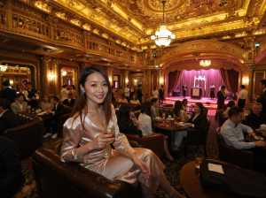 高級レストランに座ってワイングラスを持ち、カメラに向かって微笑む女性を正面カメラのア...。