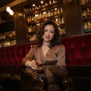 手にウイスキーのグラスを持ち、バーに座っている中年のアジア人女性のポートレート。